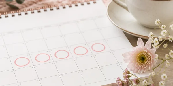 Calendrier papier avec des jours entourés, fleurs et tasse de tisane